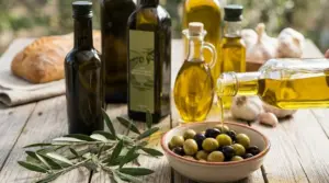 Bottiglie di olio d'oliva e ciotola di olive su tavolo rustico, con olio versato in primo piano