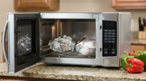 Microonde aperto con alluminio, contenitore, ciotola di vetro, cucchiaio ed uovo su un piano cucina