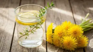 Bicchiere d’acqua con limone ed erbe aromatiche accanto a fiori gialli, rimedio naturale per la vescica