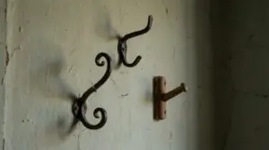 Vecchi ganci in metallo e un appendino in legno fissati a una parete usurata di una casa antica