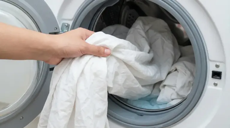 Una mano inserisce lenzuola bianche nella lavatrice per un lavaggio efficace contro acari e batteri