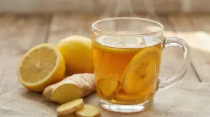 Tisana calda allo zenzero e limone in tazza di vetro con fette di limone e radice di zenzero